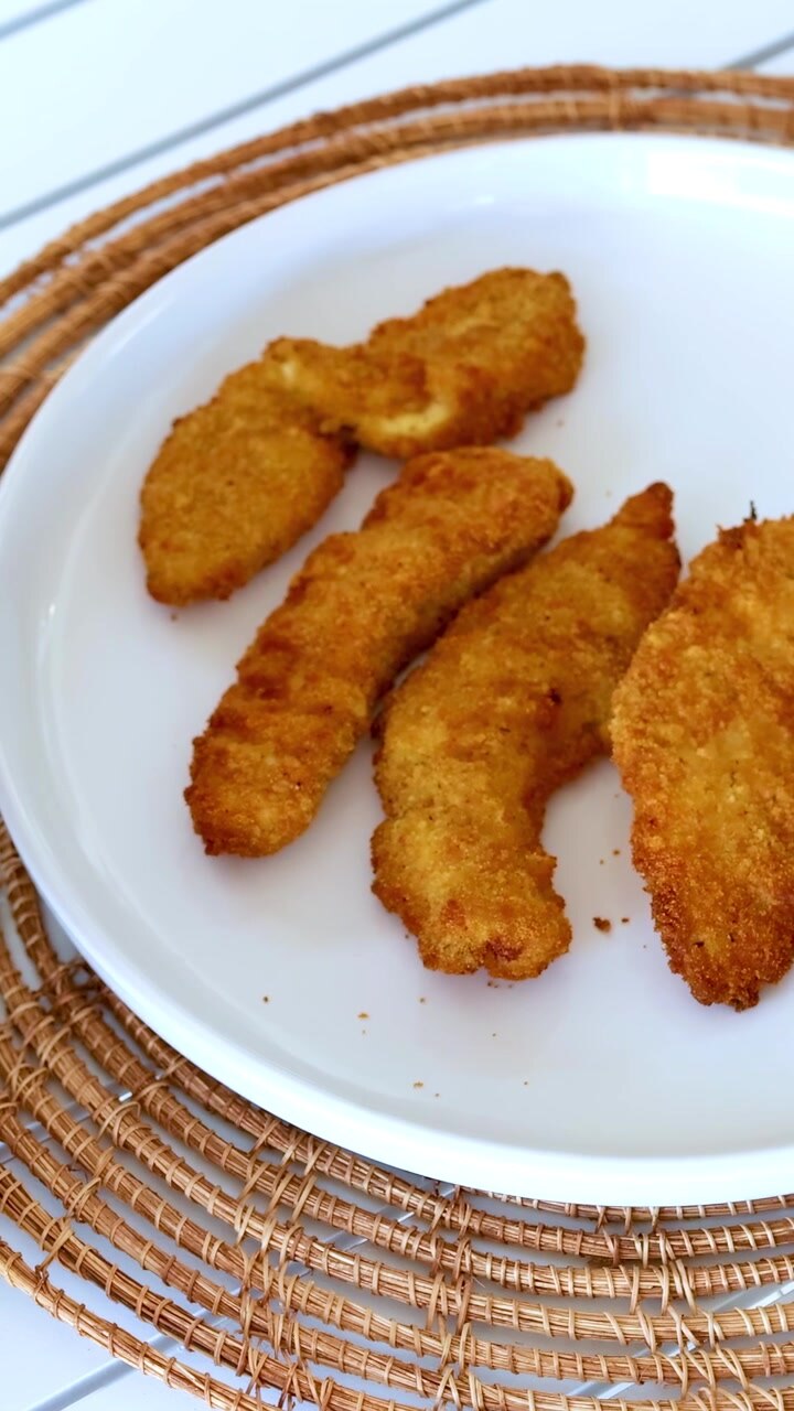 Golden chicken strips are removed from an air fryer and placed on a plate in a bright kitchen setting