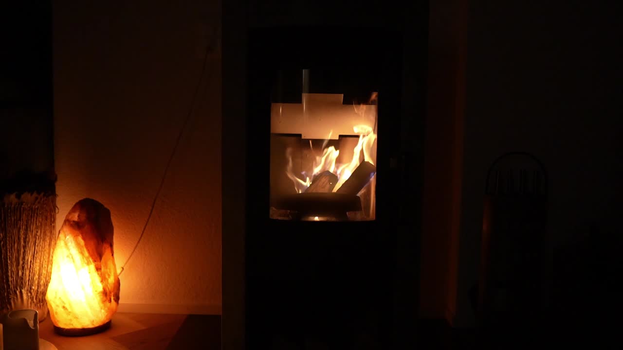 A warm and inviting scene with a cozy fireplace casting a warm glow on the room. The flickering flames dance within the hearth, illuminating a nearby salt lamp that emits a soft, rosy light.