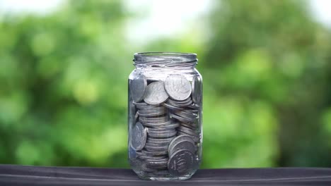 coins falling into a glass full of coins with blur green nature background. business concept, profit and saving.