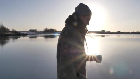 Follow-shot-of-young-male-travel-walking-at-scenic-lake-while-drinking-coffee