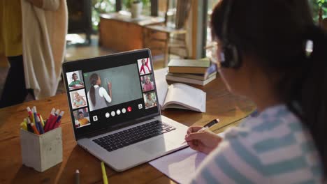 Girl-doing-homework-and-having-a-video-conference-with-teacher-and-classmates-on-laptop-at-home