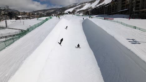 Excelente-Vista-Aérea-De-Personas-Esquiando-Y-Haciendo-Snowboard-En-Un-Medio-Tubo-En-Steamboat-Springs,-Colorado-One-Snowboarder-Falls