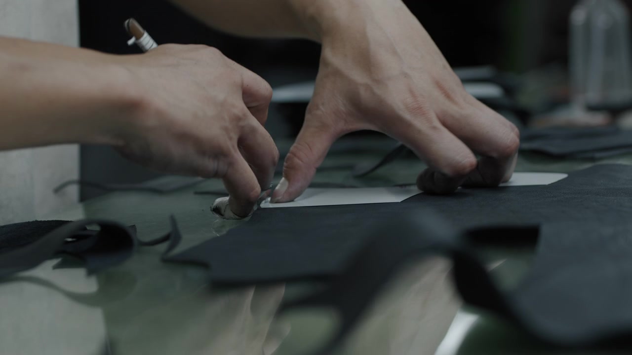 Hands cutting and arranging leather shoe pieces on a worktable in a workshop