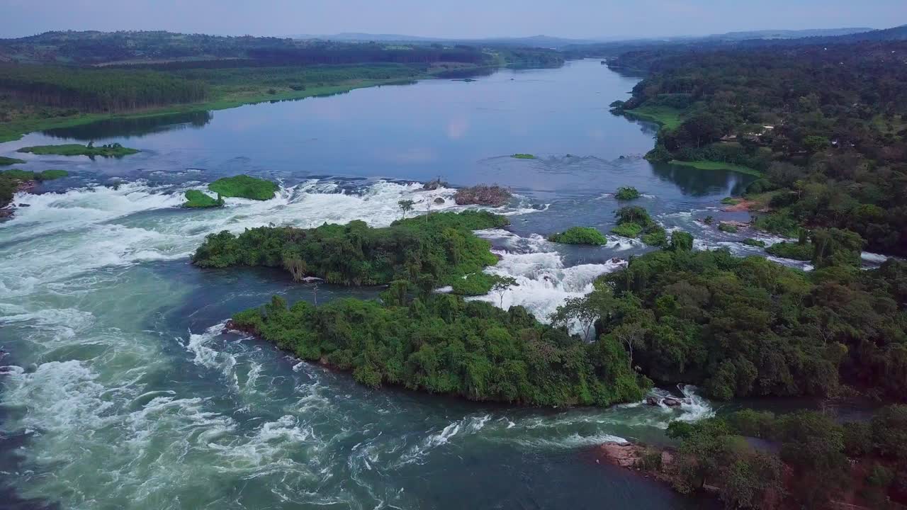 Aerial view of the source of the Nile River, with whitewater rapids flowing through lush green islands and forests in Jinja, Uganda, a popular destination for rafting and kayaking, slow motion