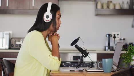 persona de raza mixta de género fluido grabando un podcast usando una computadora portátil leyendo notas en casa