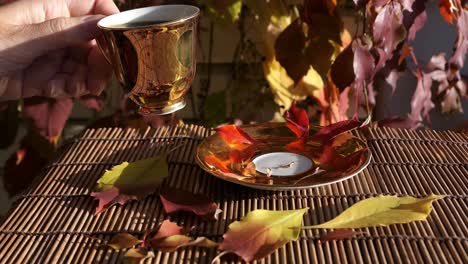 mujer bebiendo café de una taza de café dorada con coloridas hojas de otoño