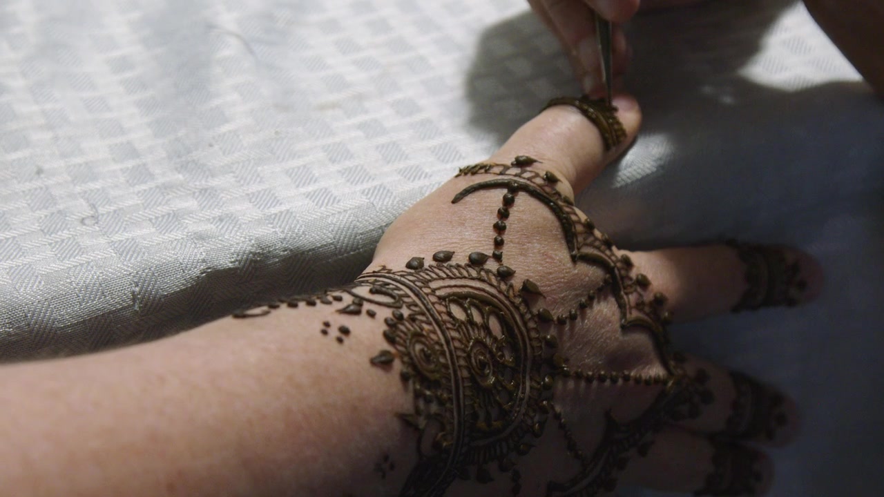 Primo piano di una macchia di henné marrone disegnata sul pollice della mano di una donna, body art
