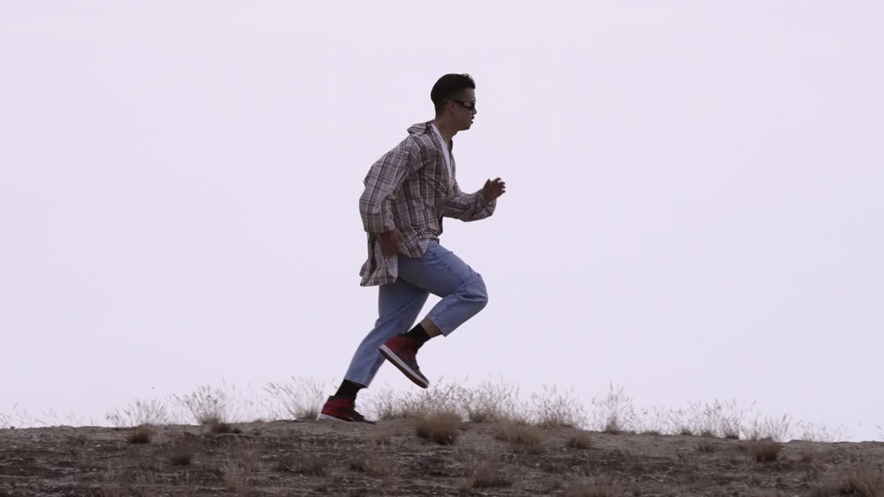 Young male model with loose casual clothing running on dry grassland. Side view. Slow motion