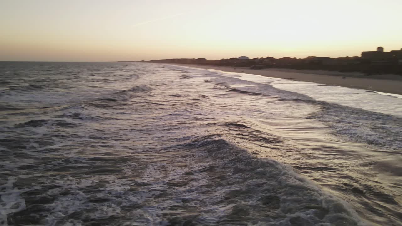 Tramonto sulla spiaggia con drone che vola tra le onde.