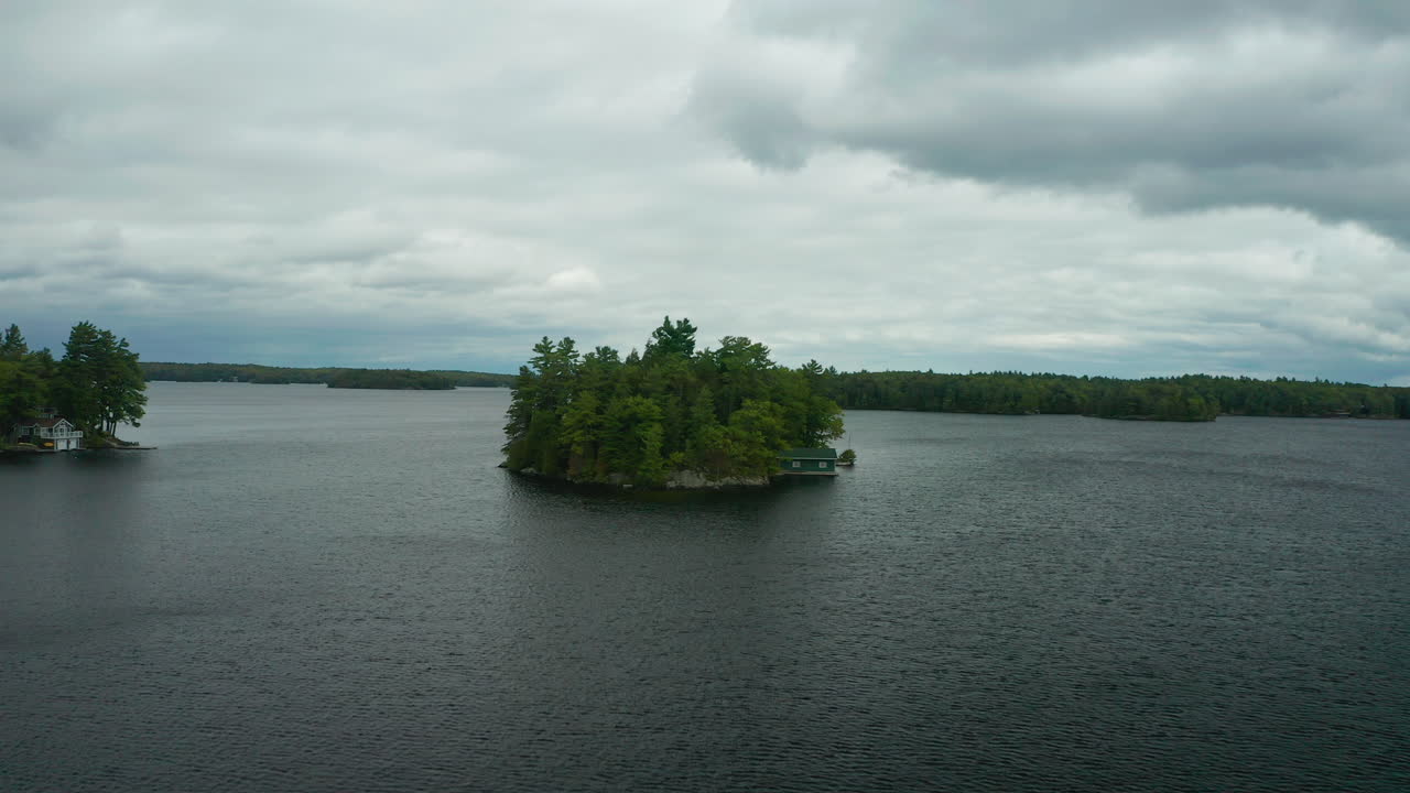 drone se acerca a una pequeña isla con una cabaña en medio del lago muskoka