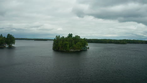 drone approaches small island with a cottage on it in the middle of lake muskoka