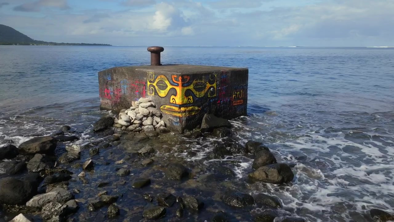 Street art a Papeete sul mare, strada di Taiarapu per Teahupoo, Tahiti Polinesia Francese, drone, Oceano Pacifico meridionale, blocco di cemento, pittura graffiti con volto polinesiano, bassa marea, rocce, onde che si infrangono, soleggiato, panoramica in avanti verso l'alto