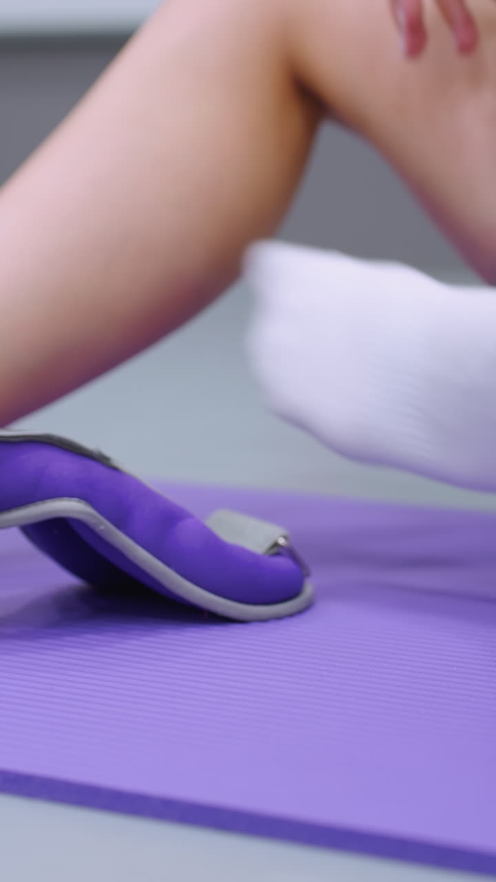 крупный план рук, расслабляющих ремень для лодыжки на белых носках, сидя на фиолетовом коврике, размытый фон намекает на среду тренажерного зала
