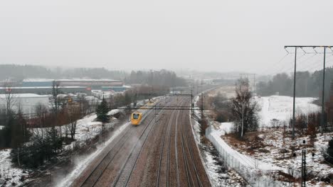 Luftaufnahme-Eines-Geschwindigkeitszuges,-Arlanda-Express-Vorbei-Unter-Drohne-In-Industrieller,-Winterlandschaft-In-Richtung-Arlanda-Flughafen