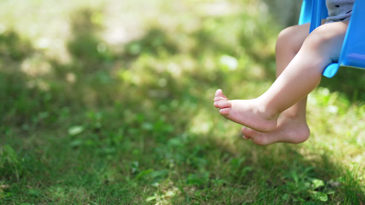 Cute little bare feet of a baby swinging on a blue swing. Happy childhood concept. Baby spending time in the nature. Blurred background.