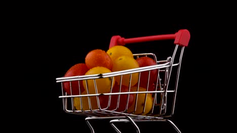 macro disparo de un carrito de compras lleno de tomates de uva rojos y amarillos amontonados con gotas de agua. girando en la mesa giratoria. aislado en el fondo negro. primer plano.