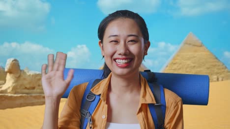 close up of asian female hiker with mountaineering backpack waving hand and saying bye while traveling in pyramid of giza