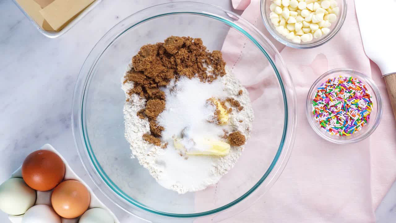 Baking confetti sugar cookies and using a white electric mixer and adding eggs to the batter. In the kitchen making a dessert. Making confetti cookies with a white background, pink napkin and eggs