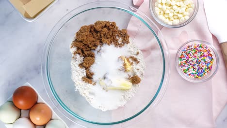 baking confetti sugar cookies and using a white electric mixer and adding eggs to the batter. in the kitchen making a dessert. making confetti cookies with a white background, pink napkin and eggs