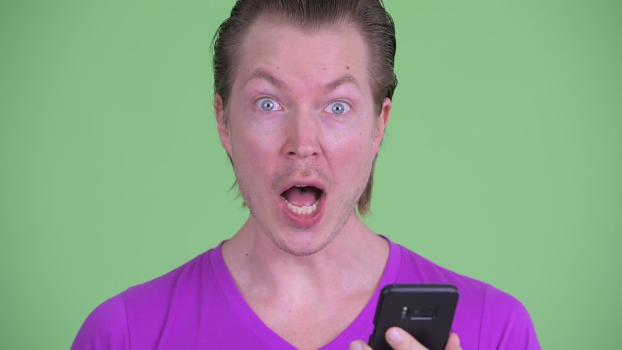 zoom en la toma de un joven que se ve emocionado mientras usa el teléfono móvil contra un fondo verde