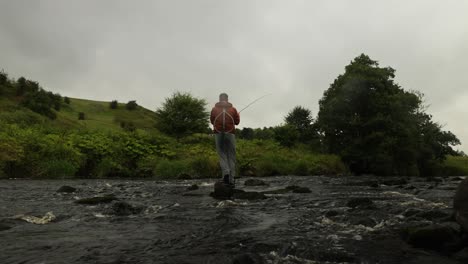 Low-angle-shot-of-a-fisherman-standing-on-a-rock-and-casting-into-a-small-stream