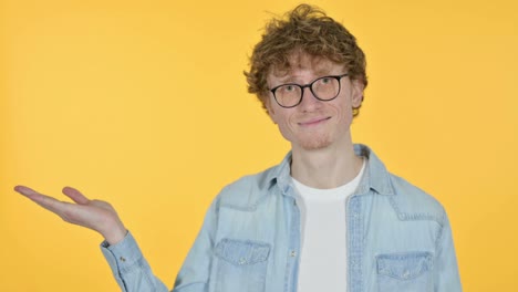 copy space, redhead young man showing product on hand, yellow background