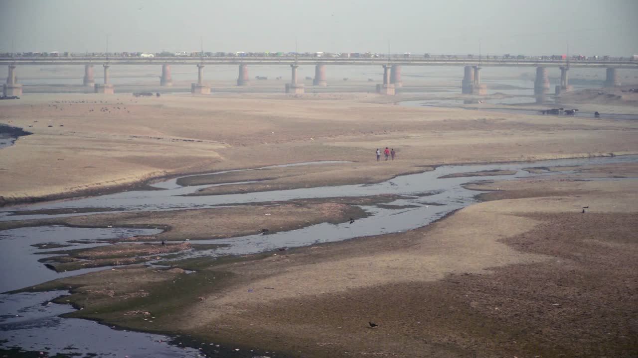 una cacerola al rio vacio con su agua estancada y chozas de los pobres, y un puente, el con trafico, arboles, torre electrica y casas con el rio