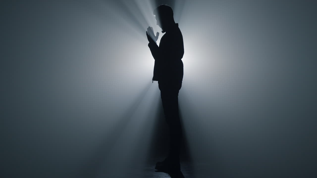 어 ⁇  속에서 기도하는 남자. 실루 ⁇  믿는 사람이 손을 맞대고 기도합니다.