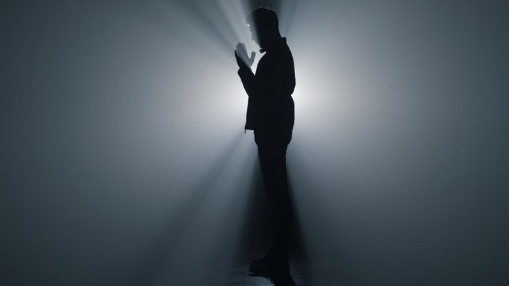 Full length praying man in darkness. Silhouette believer folding hands prayer.