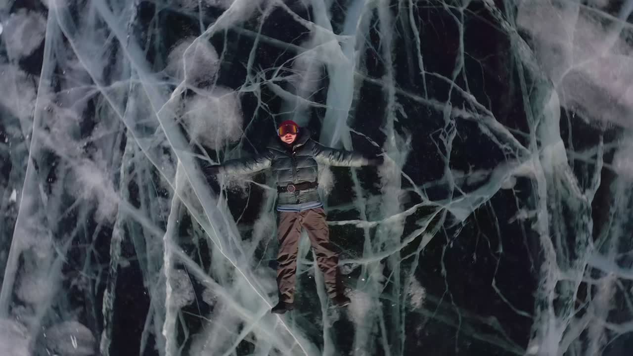 дрон вращается и уходит. девушка лежит на льду зимой, размахивая руками и ногами в сторону, изображая ангела.