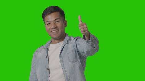 studio shot of casually dressed young man giving thumbs up gesture against green screen 1