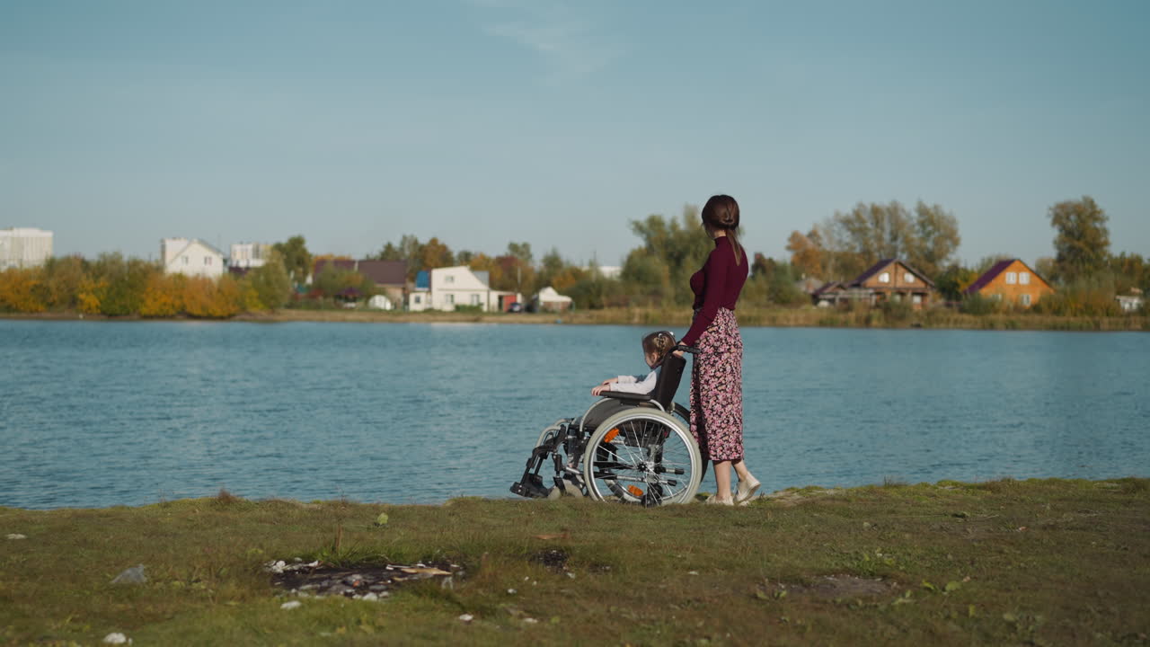 madre e hija en silla de ruedas caminan por la orilla del lago