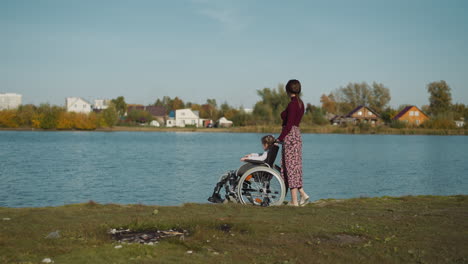 mother and daughter in wheelchair walk on shore of lake