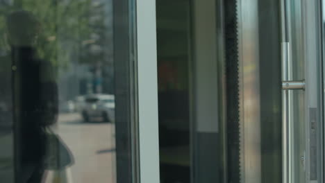 professional banker opens glass door walking out of building with her reflection visible on door, parked cars in background, urban setting, focus on business attire, and modern environment