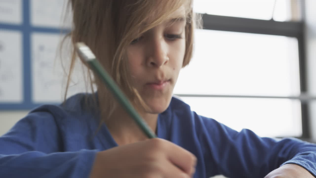 In school, child concentrating on writing with pencil in classroom