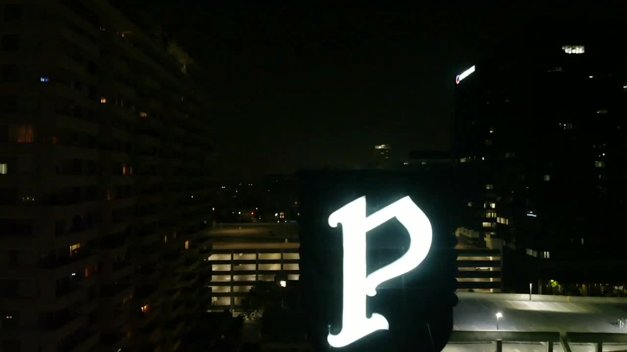 toma nocturna de ariel volando sobre un letrero iluminado de una letra p gigante en un área urbana de la ciudad