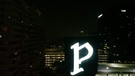 ariel night shot flying above a lite up sign of a giant letter p in a city- urban area