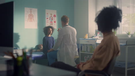 man doctor checking preteen kid reaction in office clinic. african mom waiting.