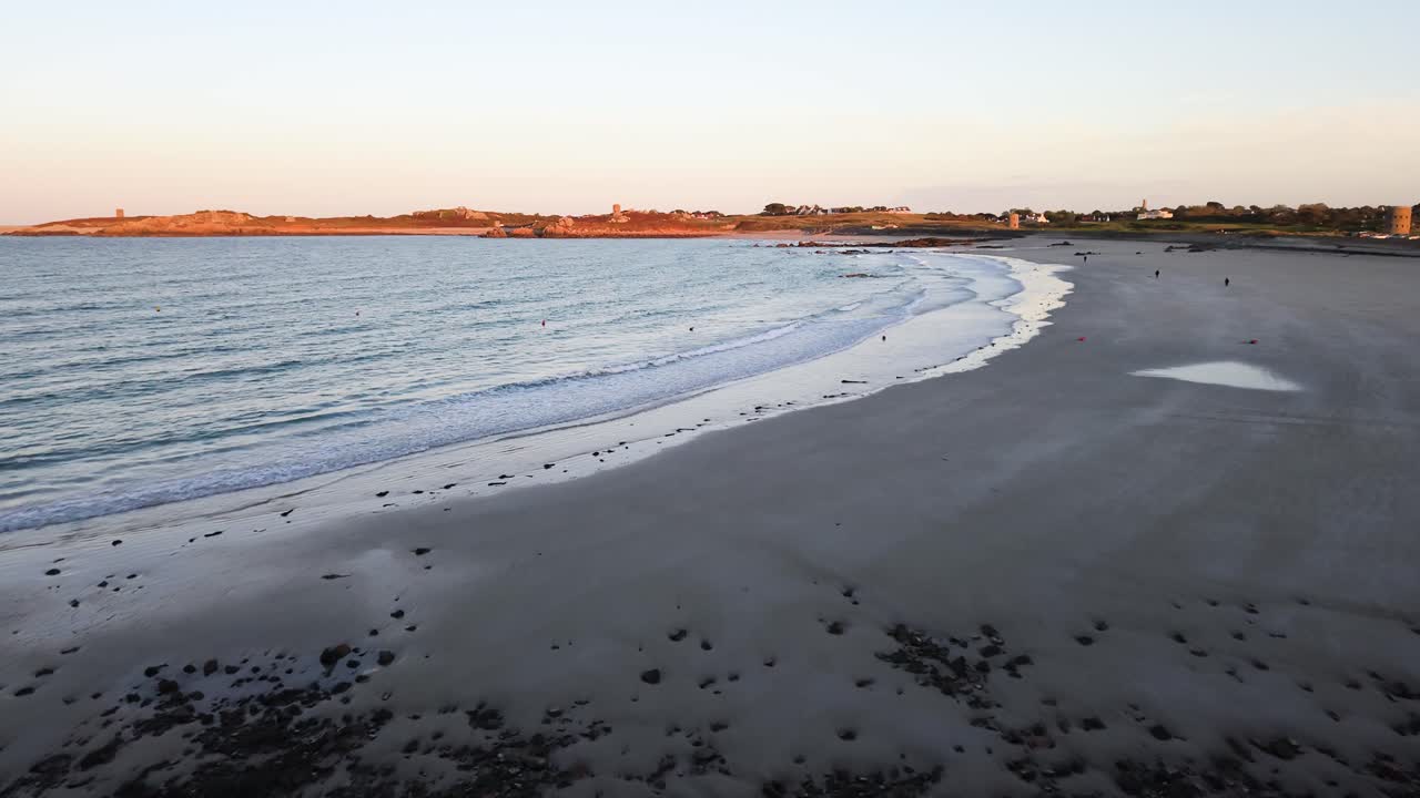 Lancresse Bay Guernsey Channel Islands low flight over shoreline of perfect sandy beach with gentle waves in the golden hour with clear sky and calm sea