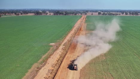 tractor pulling small road grader causes dust to billow over the crop