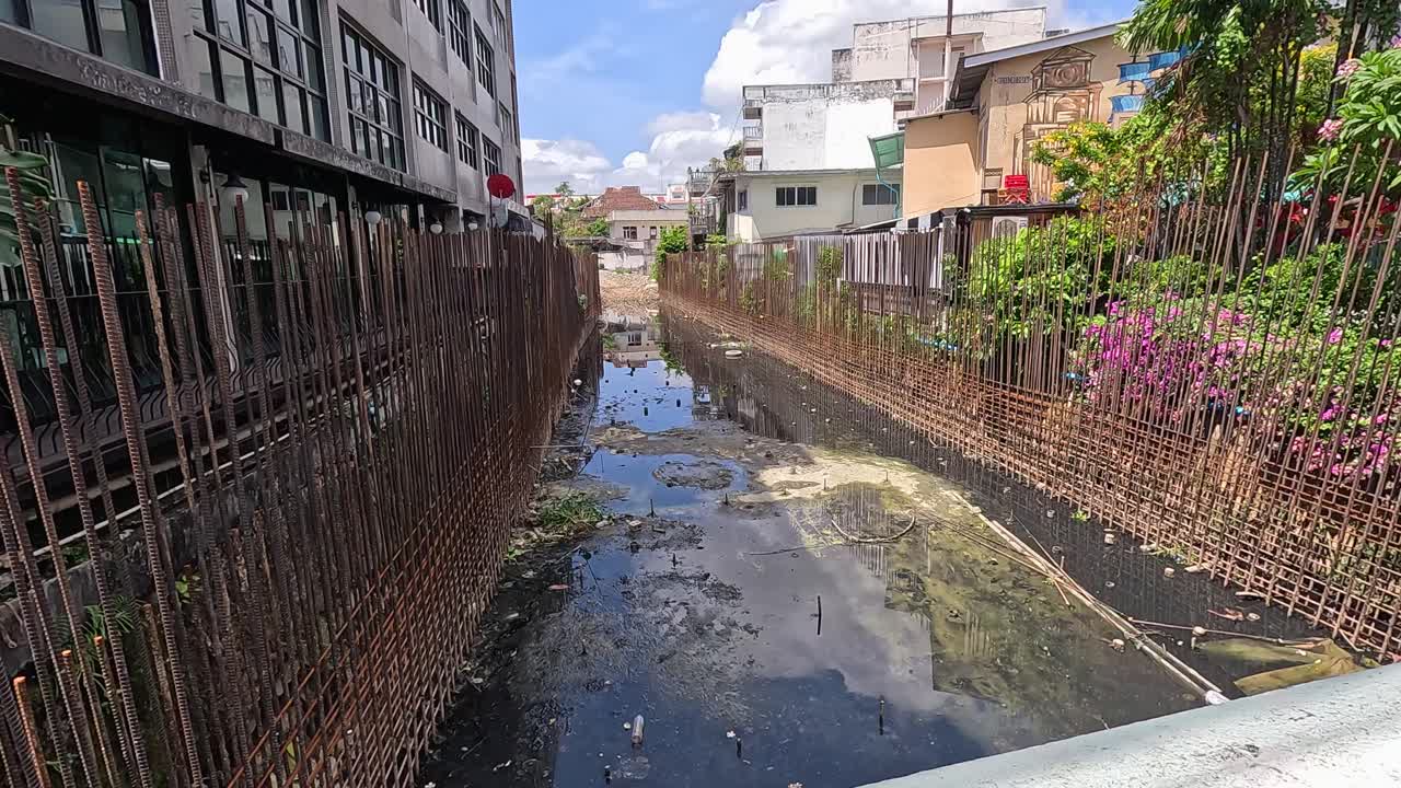 A canal in an urban setting shows visible pollution and chemical waste under bright daylight, highlighting environmental concerns