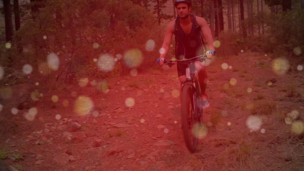 Mandlig cyklist kommer ind, cykler ned ad en skovsti til sport, mens et rødt bokeh-overlay fremhæver bevægelse