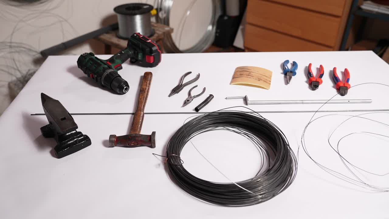 Totalbillede af værktøj, ambolt, hammer, tang og ståltråd klargjort til traditionelt slovakisk trådarbejde. Værkstedsopsætning til drotarstvo metalarbejde og produktion af håndlavet folkekunst.
