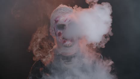 zombie man with makeup with wounds scars and white contact lenses blows smoke from nose and mouth