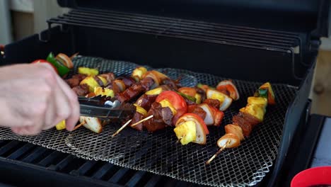 shish kabobs on a grill, caucasian hand turning chicken, steak, pineapple skewers with tongs