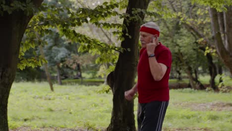 male senior person running along the road in park. mature runner man training, listening music