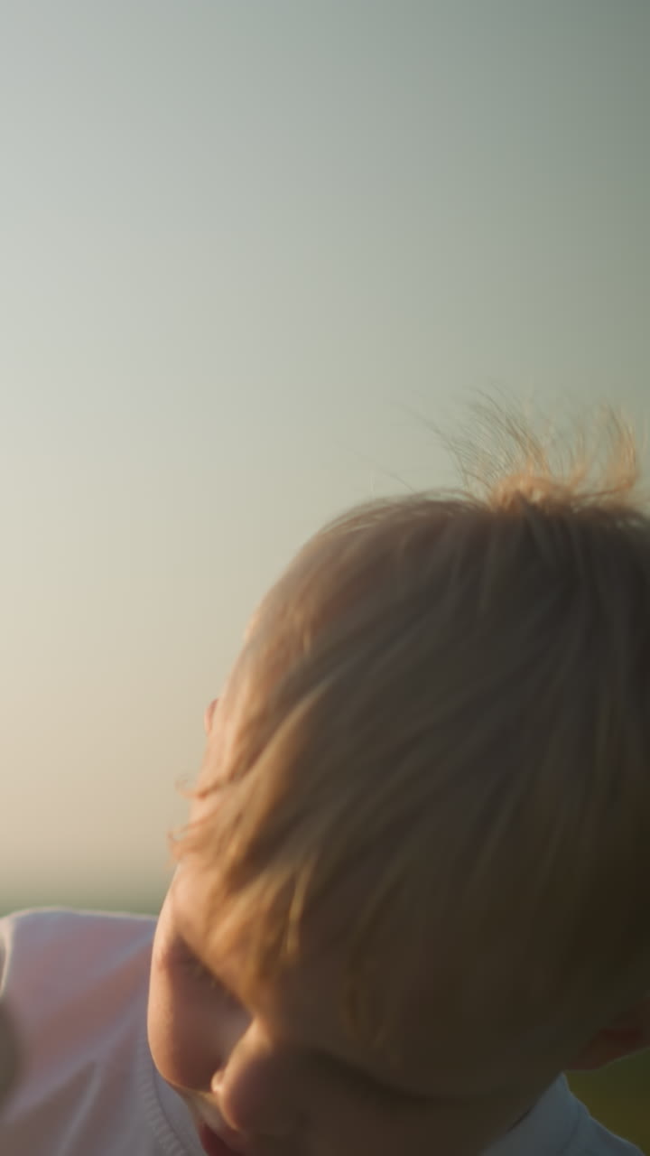 색 셔츠를 입은 어린 소년이 엄마와 함께 거품을 불어넣는 가 따뜻한 클로즈업입니다. 해가 지면 따뜻하고 황금빛으로 여 어머니와 아이 사이의 부드러운 순간을 향상시니다.