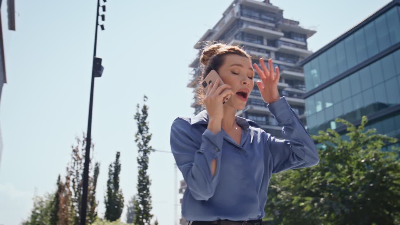 스트레스를 받은 사업가 여성이 도시 거리를 걸어다니며 전화를 하고 있습니다.