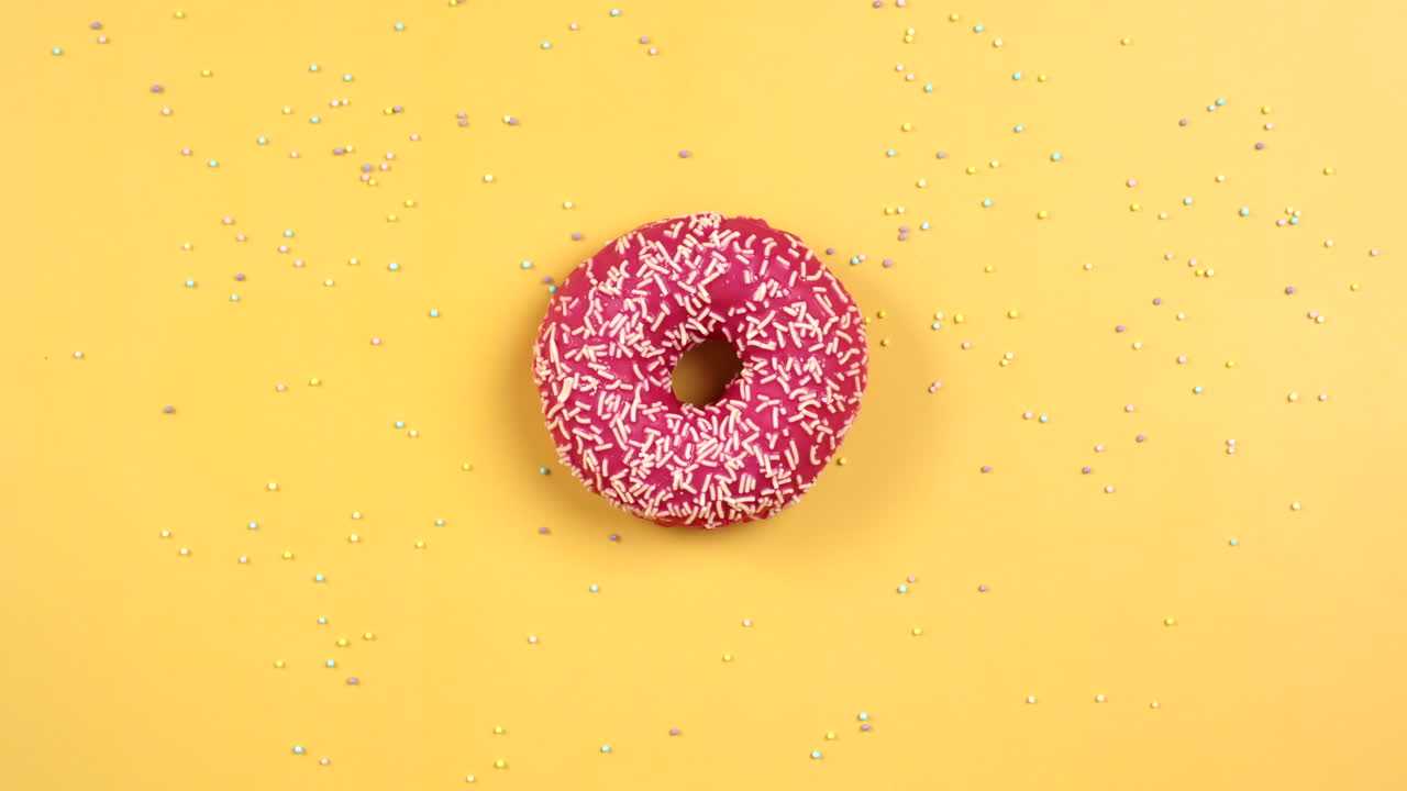 Stop motion animation of Donut rotate and got eaten. Pink Doughnut with white sprinkles on yellow background.Colorful Food animation. Concept of tasty but unhealthy snack.