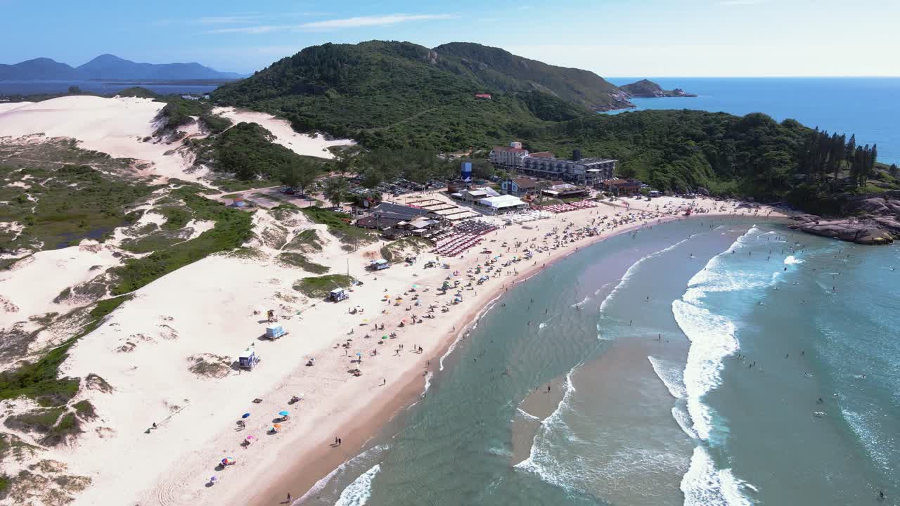 Panoramic aerial view of Joaquina Beach in Florianopolis, Santa Catarina, crowded with people and umbrellas on a sunny summer day with turquoise blue sea